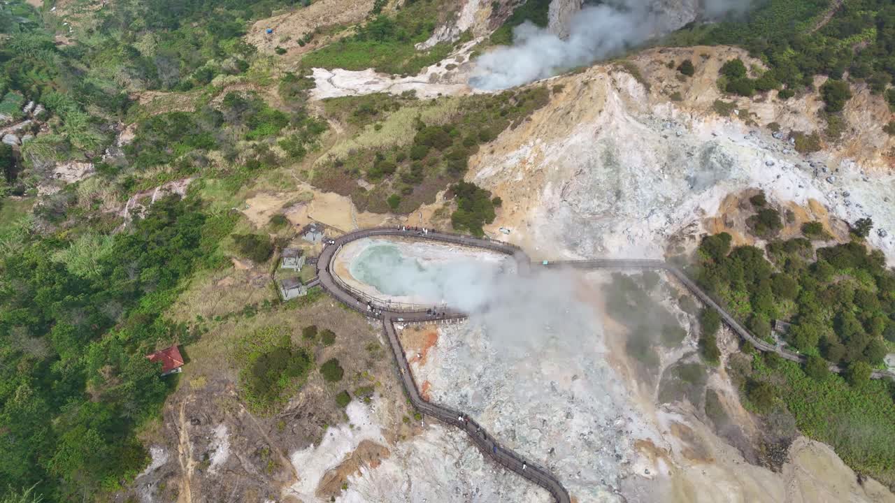 Aerial shot of the bubbling hot sulfur pond and steaming vents at Sikidang Crater, Dieng Plateau, Indonesia, set against dramatic volcanic scenery