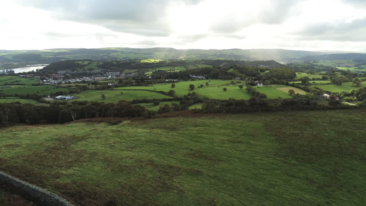 Sunbeams moving across overcast British agricultural rural village countryside morning aerial slow pan right view