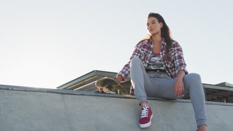 caucasian woman, sitting and holding skateboard at a skatepark