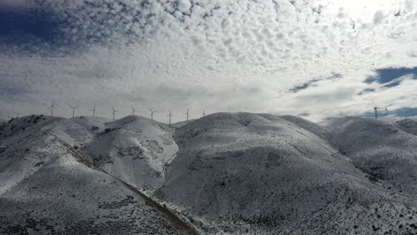 Volando-Lateralmente-Por-Montañas-Nevadas-Con-Hileras-De-Turbinas-Eólicas-Girando