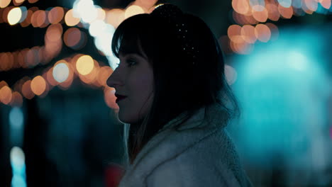 cinematic close up of a beautiful woman's face profile with orange and blue christmas lights flickering in the background during a cold winter blue hour at a christmas market