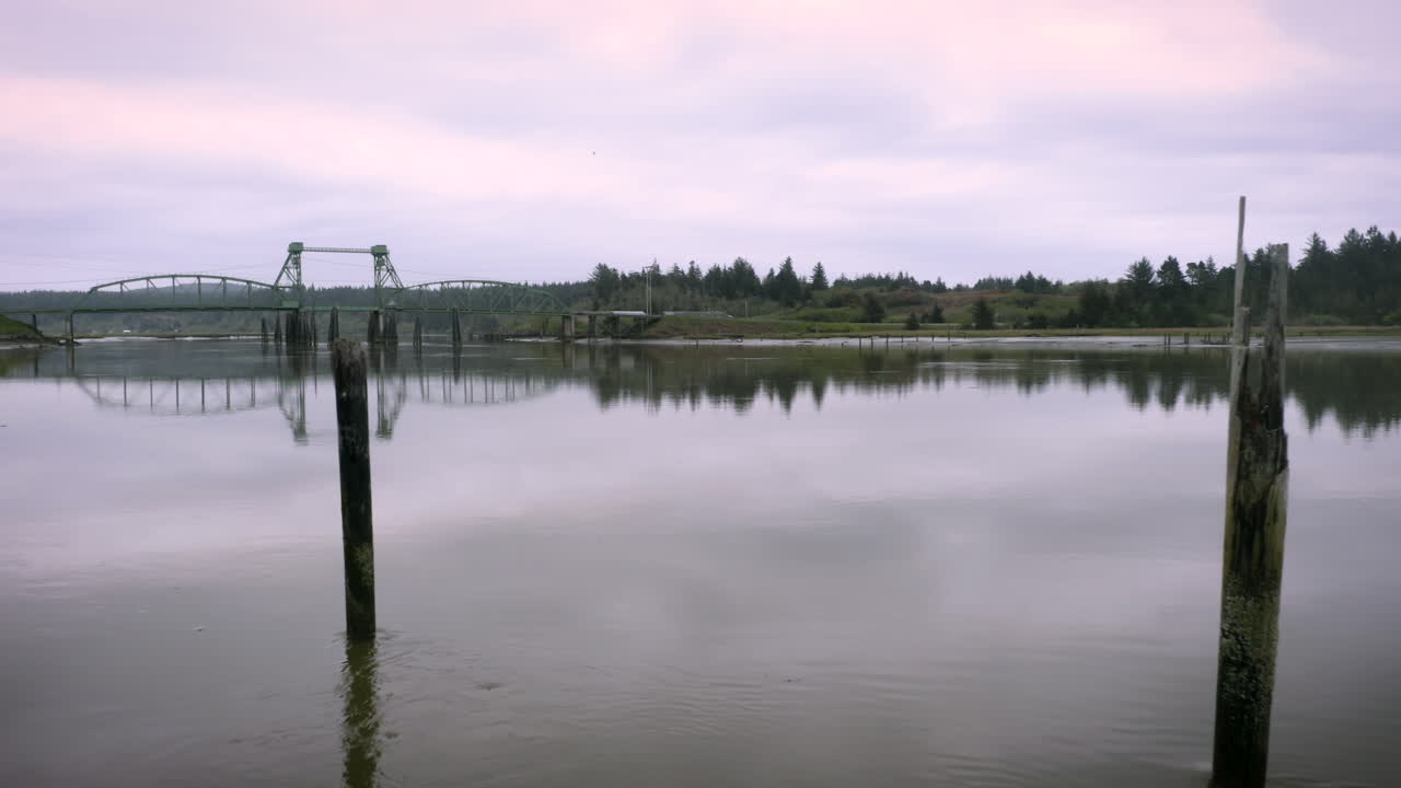 drone volando bajo sobre el río coquille entre dos postes de madera, colores rosa amanecer