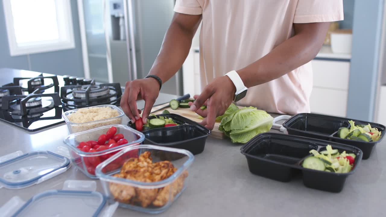 Afroamerikansk mann lager lunsjer hjemme, starter med agurker i svarte matbokser.