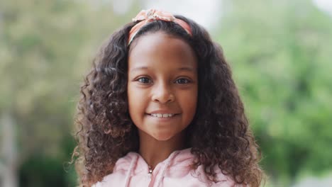 Video-portrait-of-happy-african-american-girl-with-long-curly-hair-smiling-to-camera-in-garden
