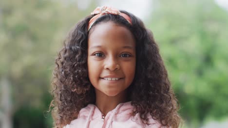 retrato de video de una feliz chica afroamericana con el cabello rizado largo sonriendo a la cámara en el jardín