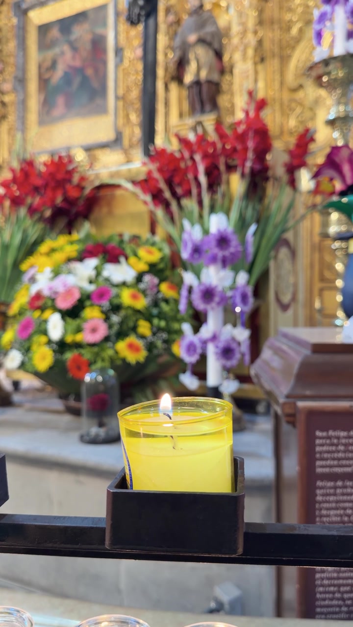 Candela gialla accesa sull'altare della chiesa con composizioni floreali colorate sullo sfondo