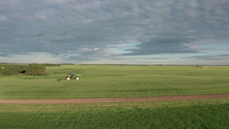 Espectacular-Vuelo-Panorámico-Sobre-Tierras-De-Cultivo-Verdes-Por-Máquinas-Agrícolas-Industriales-Que-Rocían-Fungicidas-En-Cultivos-De-Cereales-En-Un-Campo-Llano-Y-Expansivo,-Saskatchewan,-Canadá,-Parte-Aérea-Aérea-Lateral
