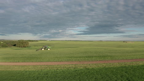 espectacular vuelo panorámico sobre tierras de cultivo verdes por máquinas agrícolas industriales que rocían fungicidas en cultivos de cereales en un campo llano y expansivo, saskatchewan, canadá, parte aérea aérea lateral