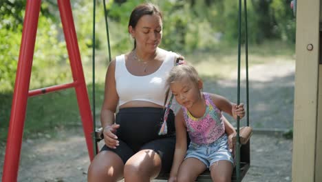 pregnant mother and daughter playing on swing outdoors