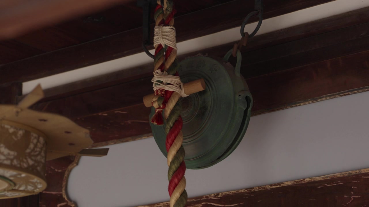 Campana di bronzo patinata e spessa corda intrecciata colorata appese sotto la gronda di un santuario giapponese