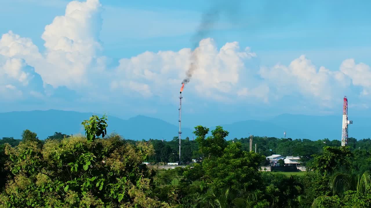Distant View Of The Flaring Tower Of An Oil Refinery Plant Surrounded By Tropical Forest. Aerial Wide Shot