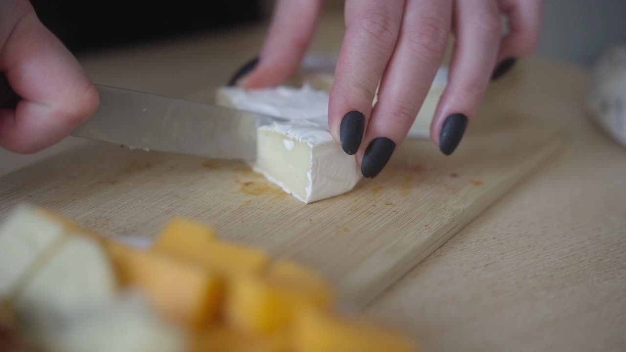A shot of a woman's hand slicing camembert cheese. Preparing cheese snacks for the evening