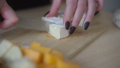 a shot of a woman's hand slicing camembert cheese. preparing cheese snacks for the evening
