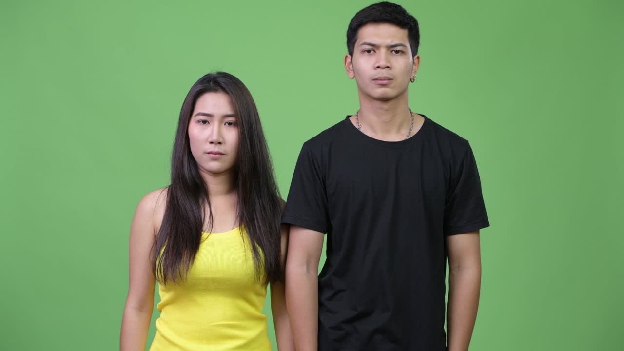 Young angry Asian couple giving thumbs down together