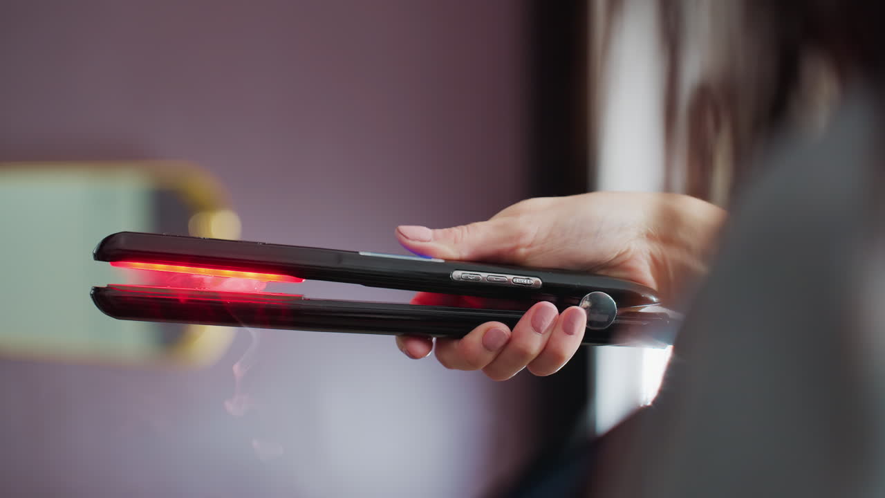estilista utilizando plancha de pelo, peluquero manejando cuidadosamente la plancha con indicador de luz roja, demostración de un dispositivo de alisado profesional con fondo de salón y técnica centrada