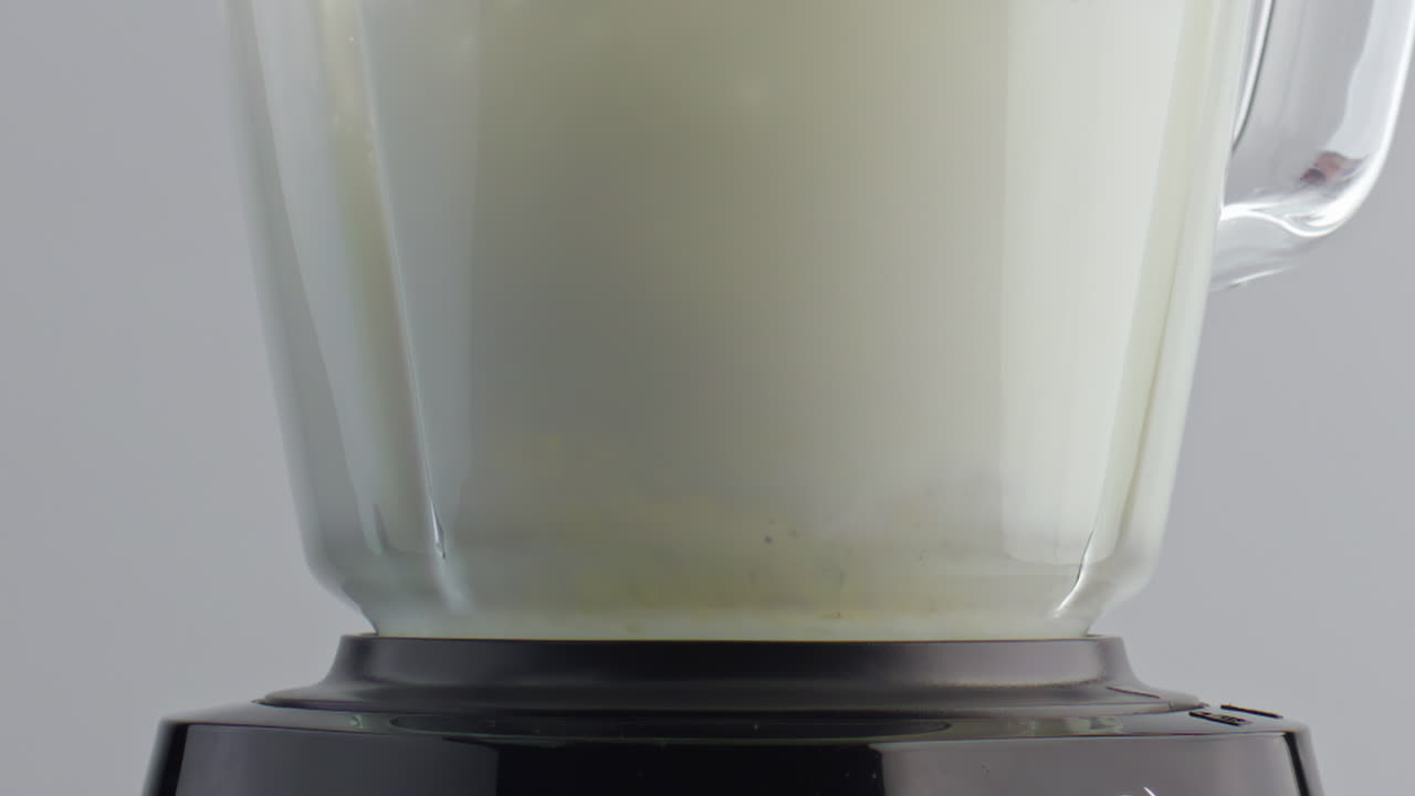 블렌더에서 신선한 우유를 슈퍼 슬로 모션 클로즈업으로 휘두르며 유제품 액체가 회전합니다.