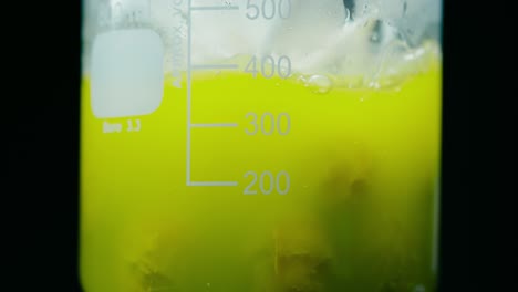 container with green liquid bubbling in a metal measuring flask