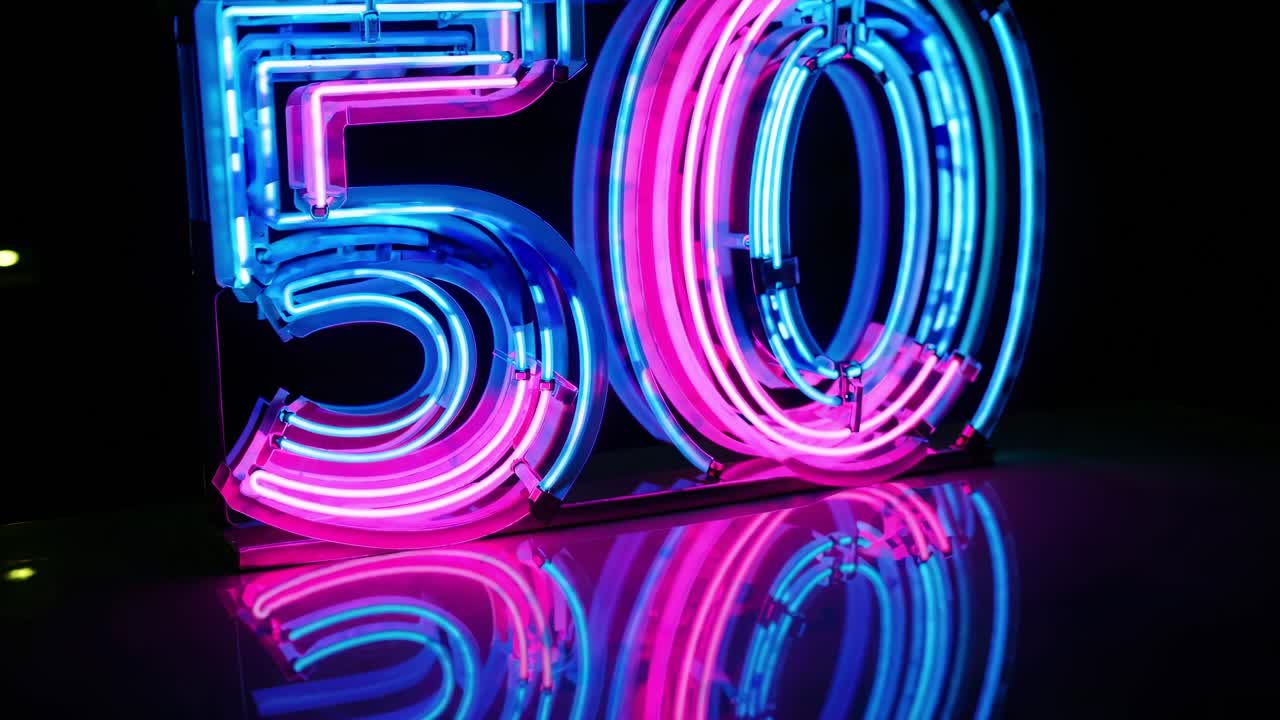 Neon number fifty glowing in pink and blue, reflecting on a dark surface, creating a vibrant and celebratory atmosphere