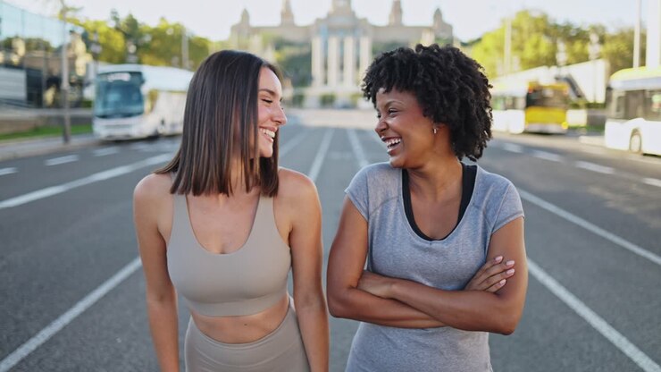 Giovani donne sorridenti in abbigliamento sportivo che stanno in piedi per strada in città