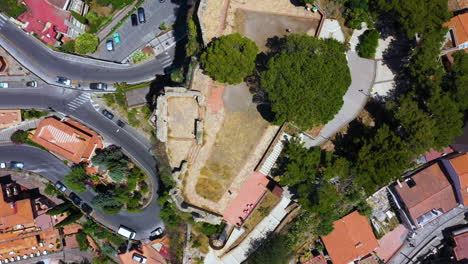 top down aerial view of the highest point on the mountain hill surrounded by winding road, orange houses and green trees