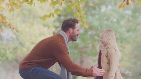 Father-Lifting-Daughter-Against-Background-Of-Autumn-Leaves-On-Countryside-Walk