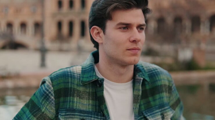 Close-up of young man turning his head and looking at camera with smile on old