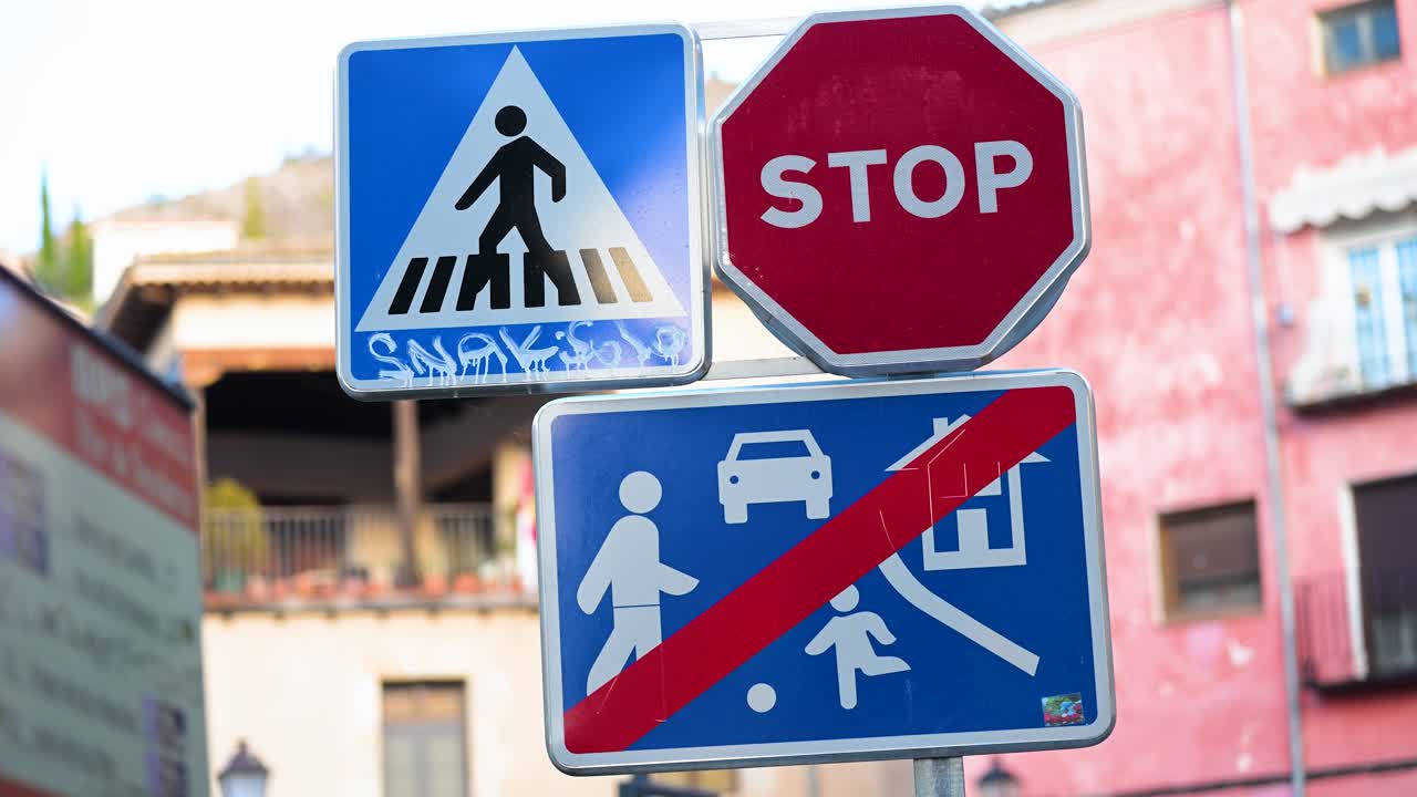 View of various traffic signs, including a red stop sign, blue pedestrian crossing sign, and 'Blue Traffic Light for Speed Limit in Residential Zone' sign on a road in Spain.