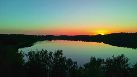 Cinematic-View-Of-A-Lake-With-Forest-Silhouettes-Reflected-On-Still-Water-During-Sunset