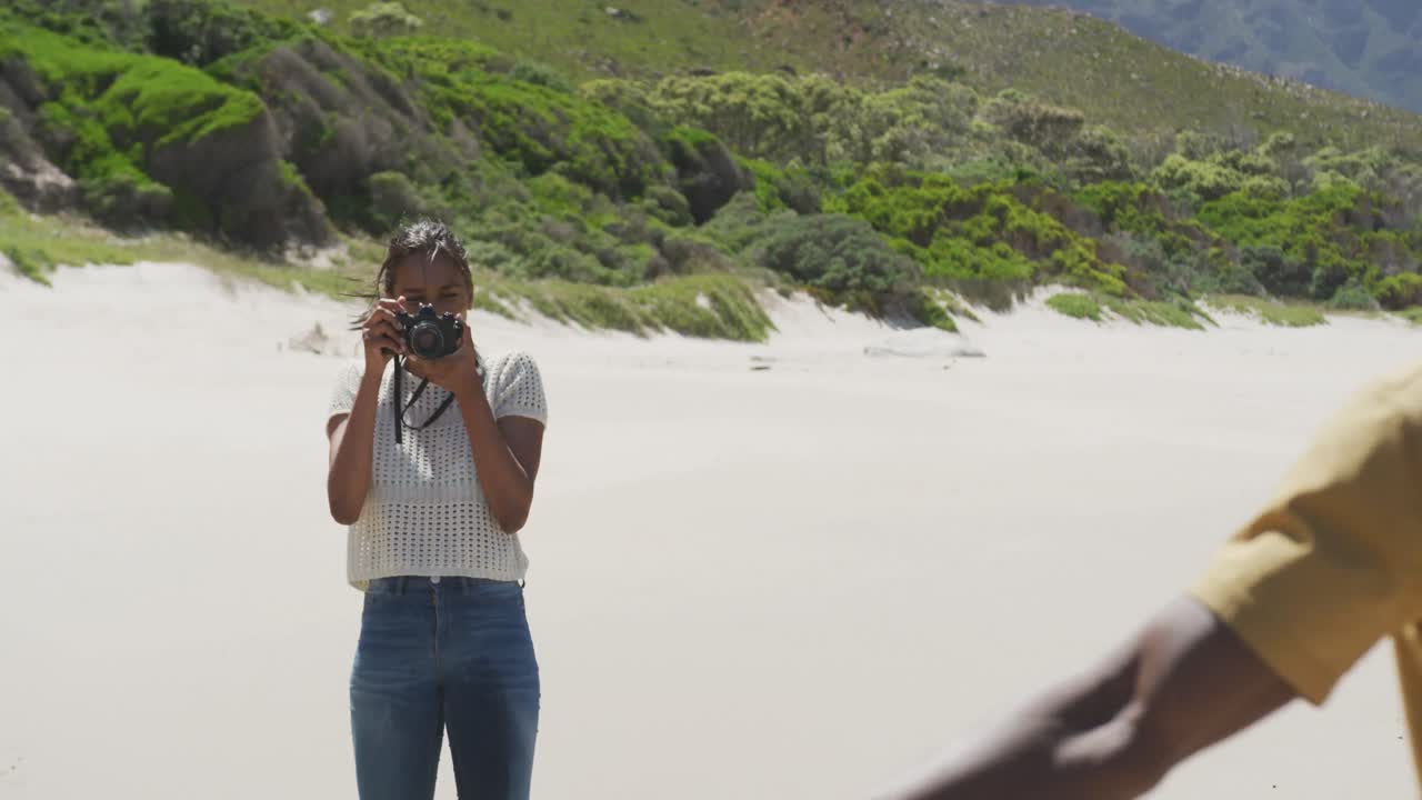 mujer afroamericana tomando una foto de su marido con una cámara digital en la playa