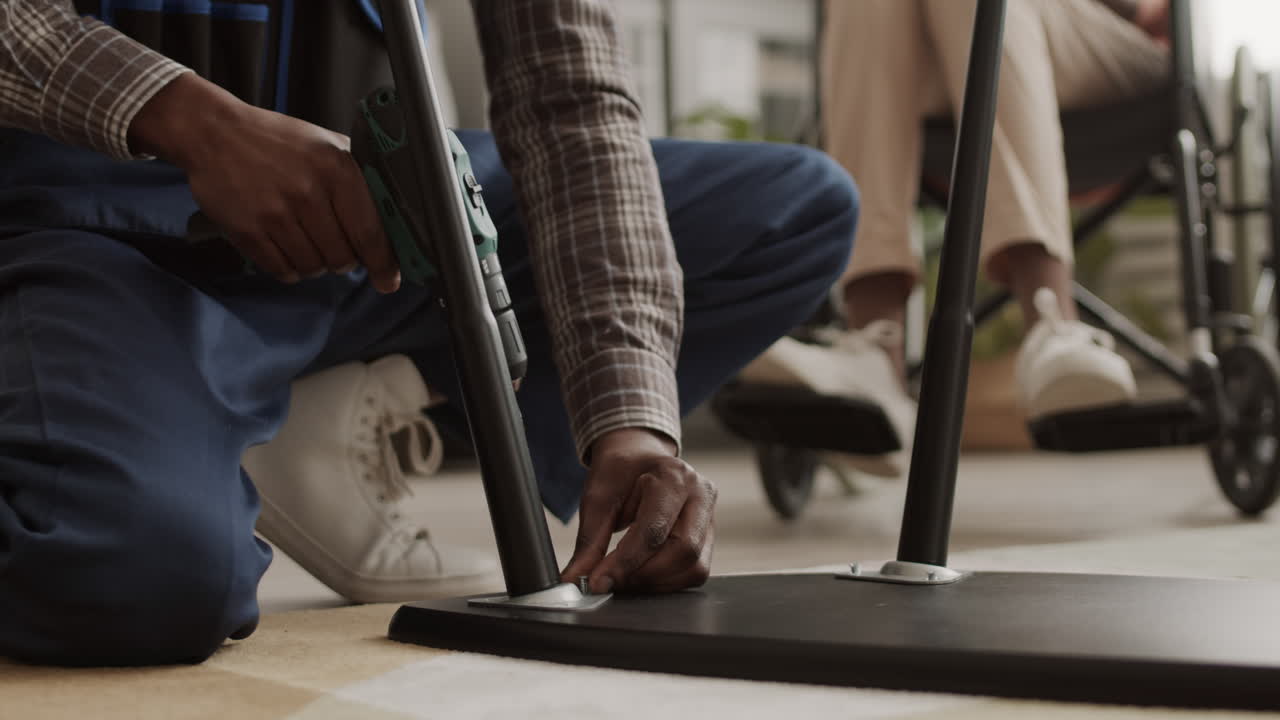Handicapped Person Watching Unrecognizable Handyman Assembling Furniture