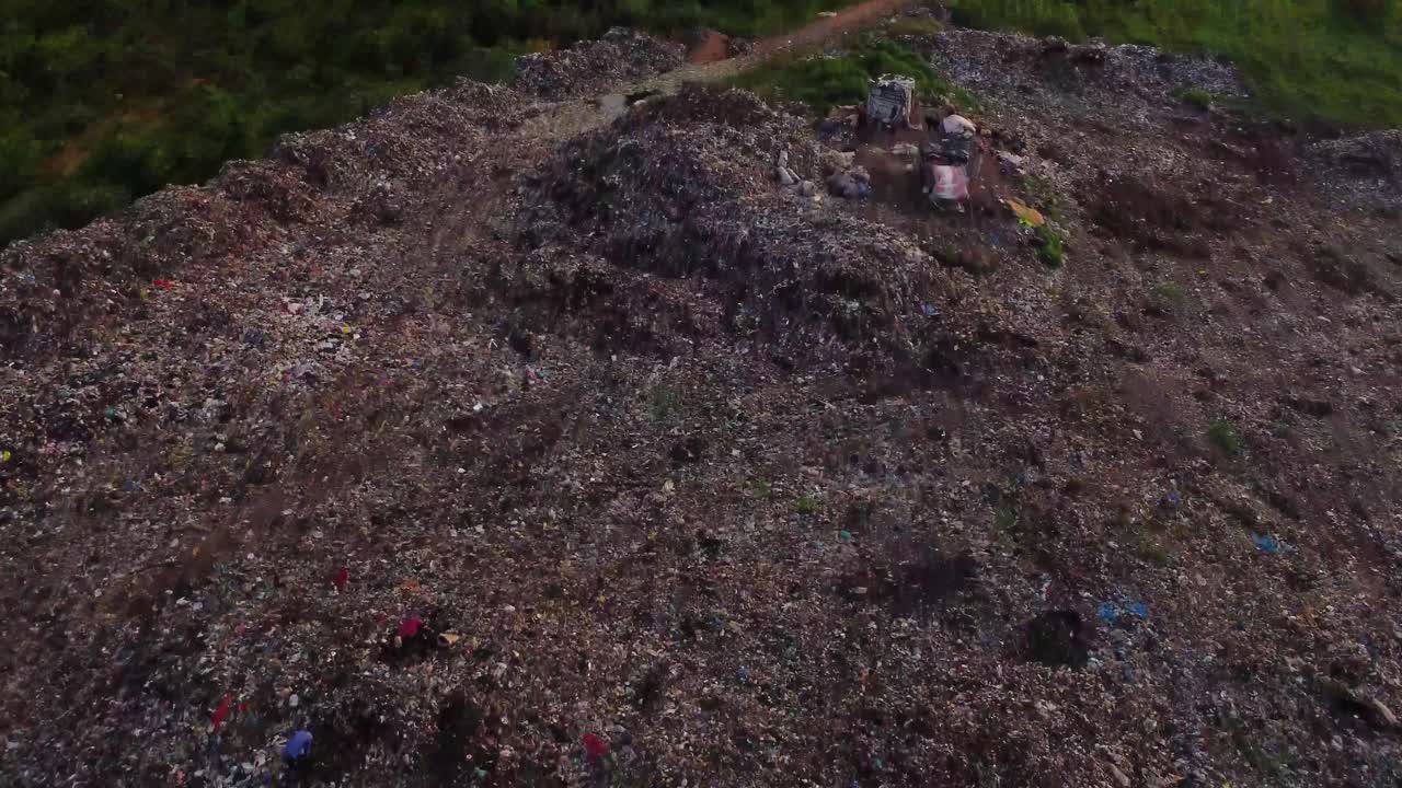 Low aerial of a large landfill polluted with garbage in a green field and waste pickers walking trough the junk