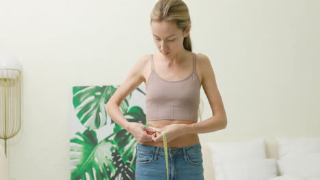 blonde woman measuring her waist in the bedroom