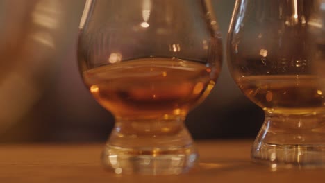 a hand sets whisky glasses on a wooden bar, warm candle-like lighting creates a cozy, intimate atmosphere with shallow depth of field and soft background blur
