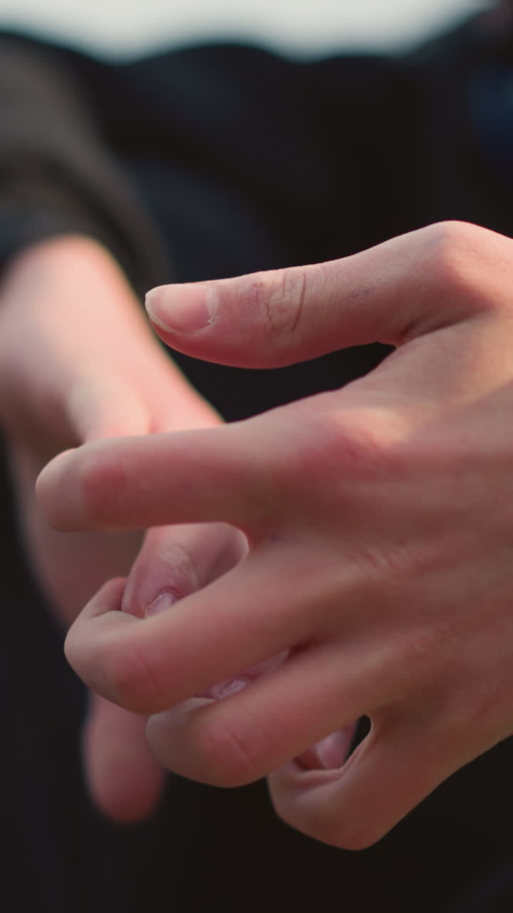 Close-up of someone clasping his hands together with a blurred background view of another person wearing a gray top by the side