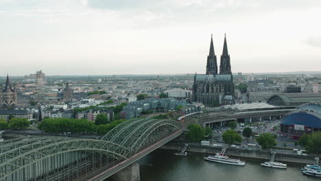 Drohne-Bewegt-Sich-In-Zeitlupe-Nach-Rechts,-Der-Kölner-Dom-Bei-Trübem-Wetter-Im-Zentrum,-Die-Hohenzollerbrücke-Mit-Dem-Rhein-Im-Unteren-Bildteil