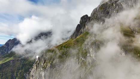 hermosa toma de drone ascendente de la ladera rocosa de la montaña en los alpes austriacos a través de nubes de niebla