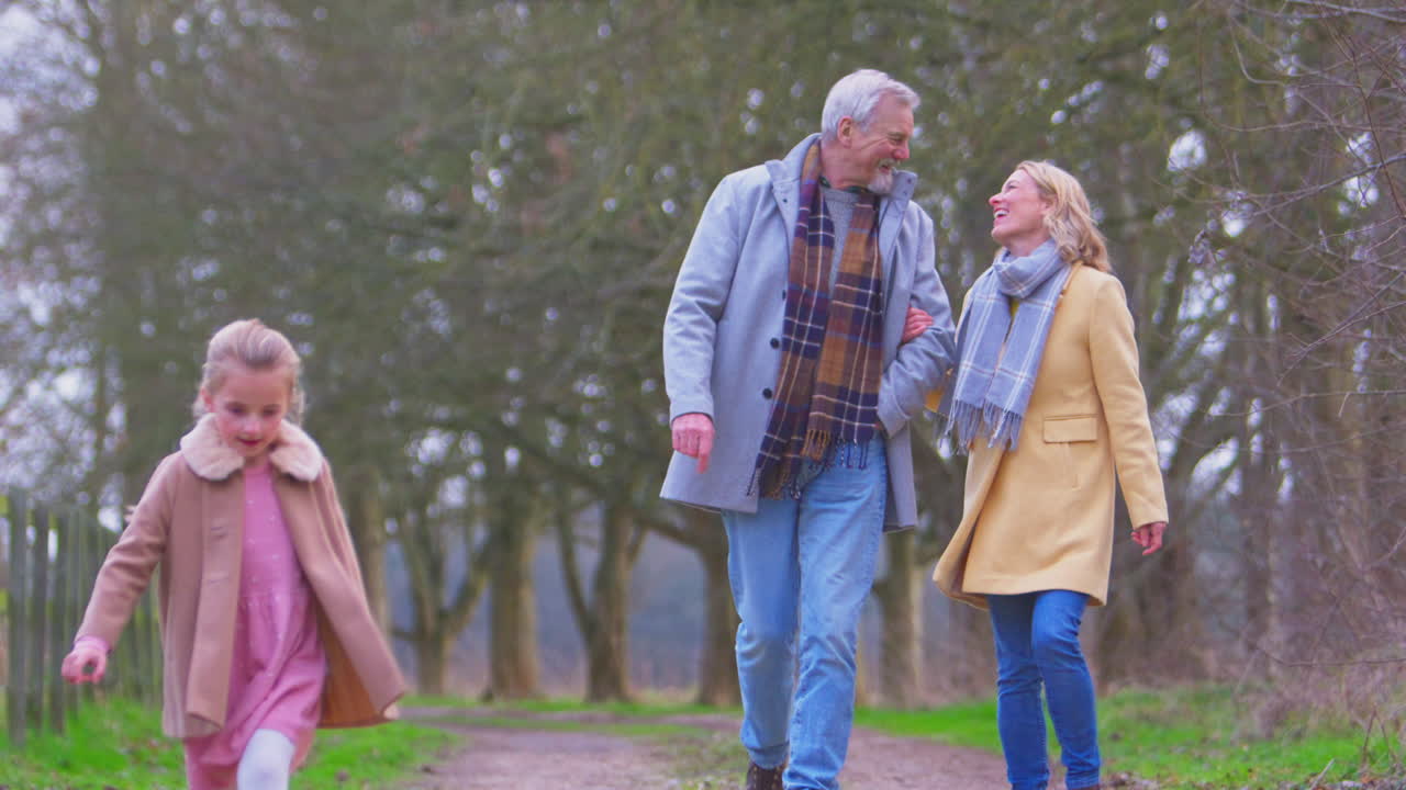 los abuelos viendo a la nieta saltar por delante en el exterior caminando por el campo de invierno
