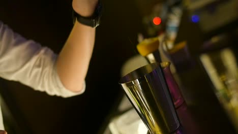 Cocktail-mix-being-poured-from-bartenders-shot-measuring-cup-into-stainless-steel-mixing-cup-filmed-as-slow-motion-close-up