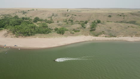 aerial side view of speed boat sailing by lake shoreline, land horizon in background in saskatchewan landing, canada