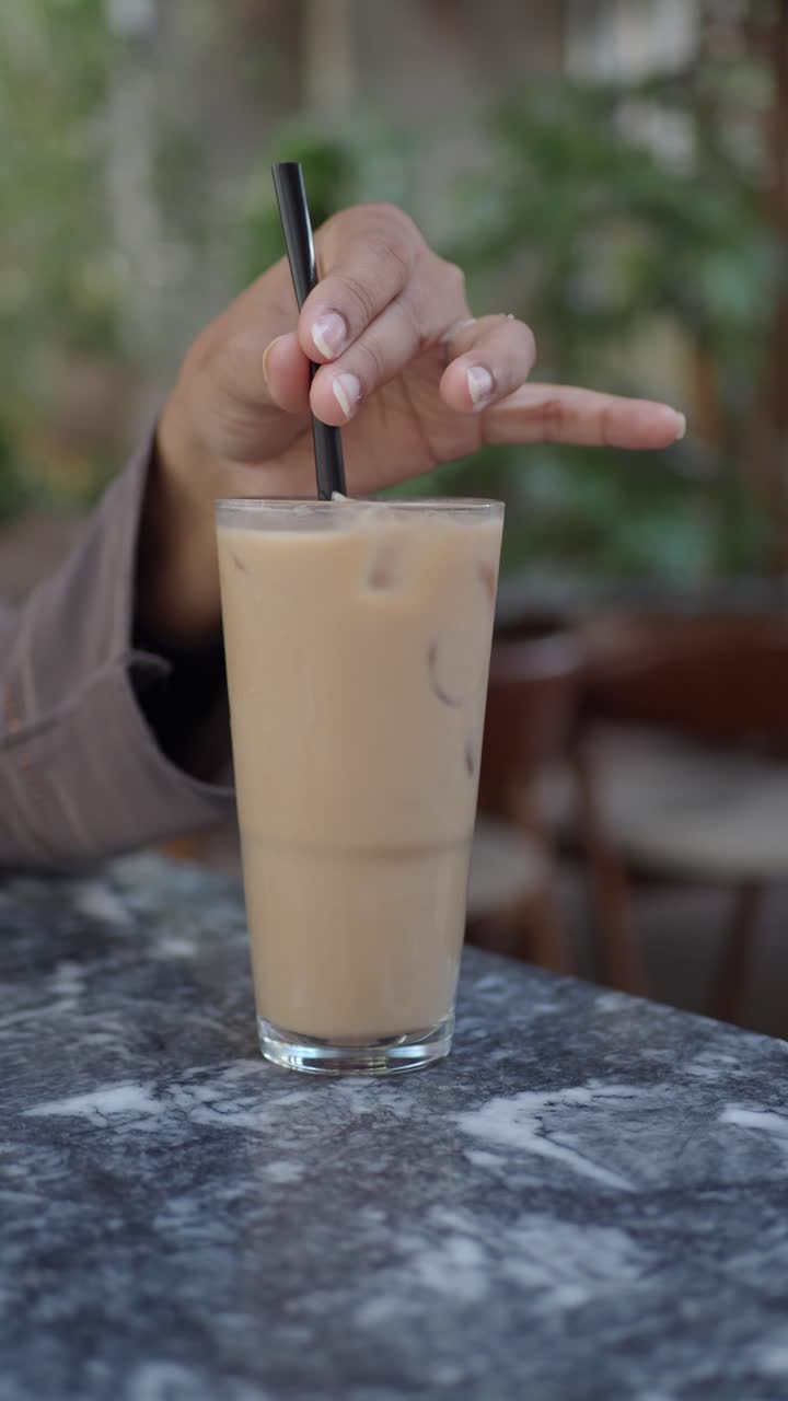 Mano che mescola caffè freddo con una cannuccia su un tavolo di marmo.