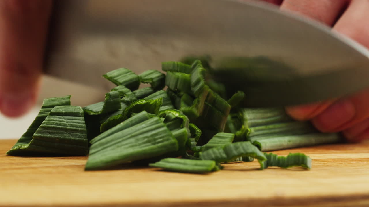 Close-up of Hand Chopping Fresh Green Leek on Wooden Board