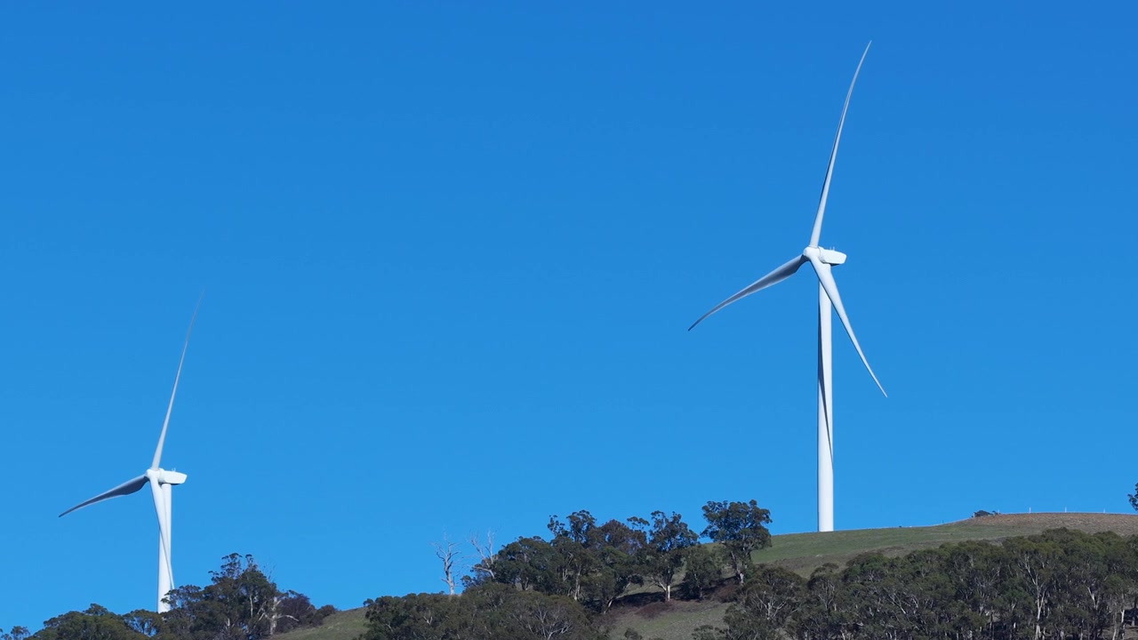 Inquadratura ampia statica di turbine eoliche bianche che girano su una cresta erbosa a Matheson, Australia