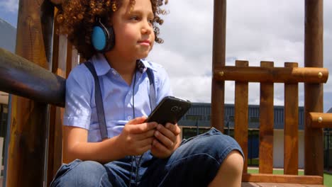 Vista-Frontal-De-Una-Colegiala-De-Raza-Mixta-Escuchando-Música-En-Un-Teléfono-Móvil-En-El-Patio-De-La-Escuela-4k