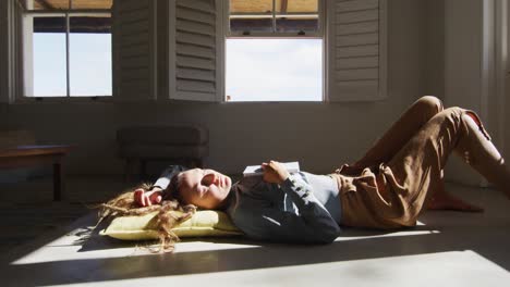Caucasian woman lying on floor holding book and sleeping in sunny cottage living room