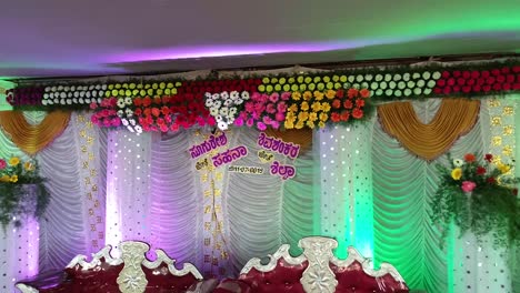 drone shot of a decorated indian wedding stage with chairs, colorful lightings, and flowers