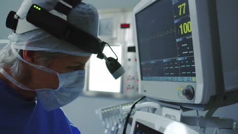 Side-view-of-Caucasian-female-doctor-operating-medical-monitor-in-operation-theater-at-hospital