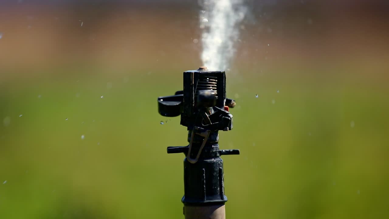 Irrigatore d'acqua che spruzza un campo agricolo durante un anno di siccità - primo piano isolato
