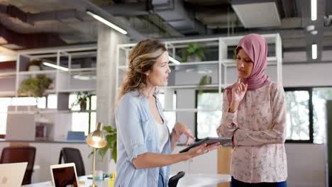 Diverse-creative-female-colleagues-in-discussion-using-tablet-in-office,-slow-motion