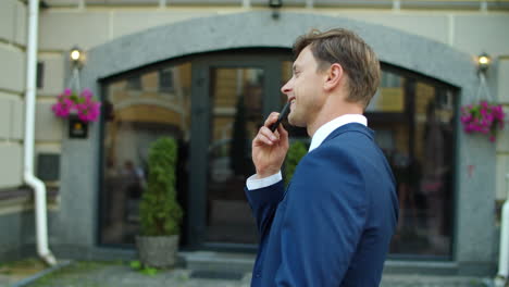 cheerful business man recording voice messages on smartphone outside