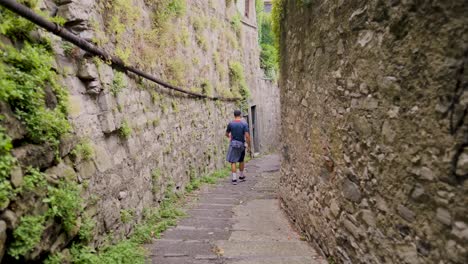 slow motion tan young man exploring as he walks down historic narrow steps shrouded by stone and plants